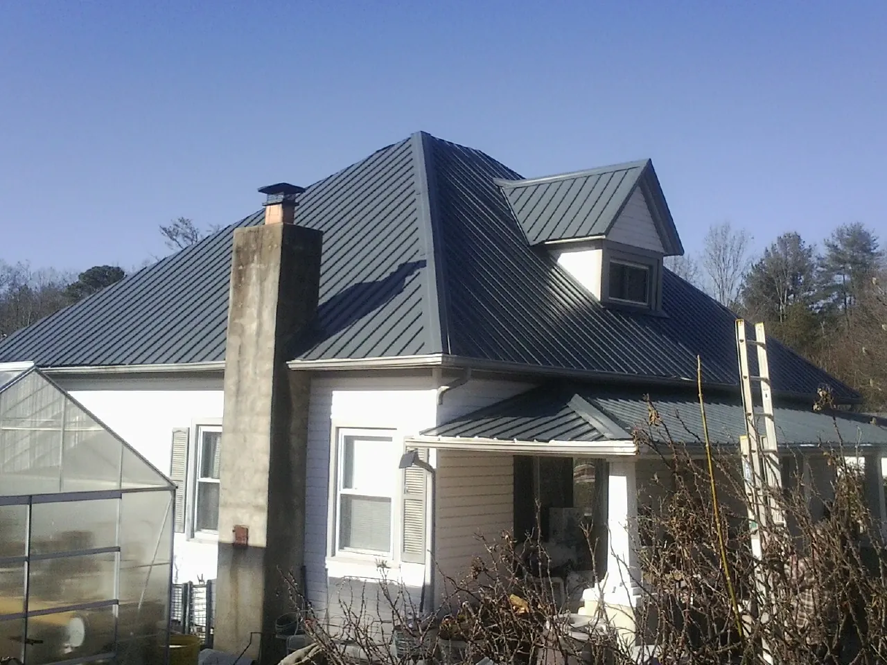 Dark blue standing seam metal roof on a white farmhouse with dormer — Slate & Tile Roof Repair by Roofing Brothers in Pomona Park
