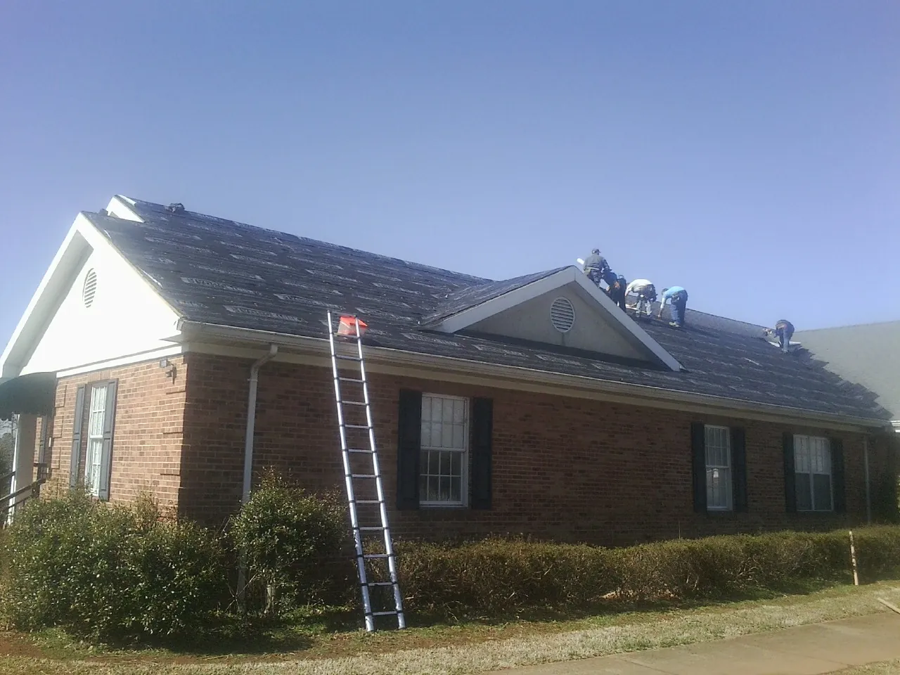 Crew tearing shingles off a brick ranch roof with a ladder set — Emergency Roof Repair work by our crew in Pomona Park