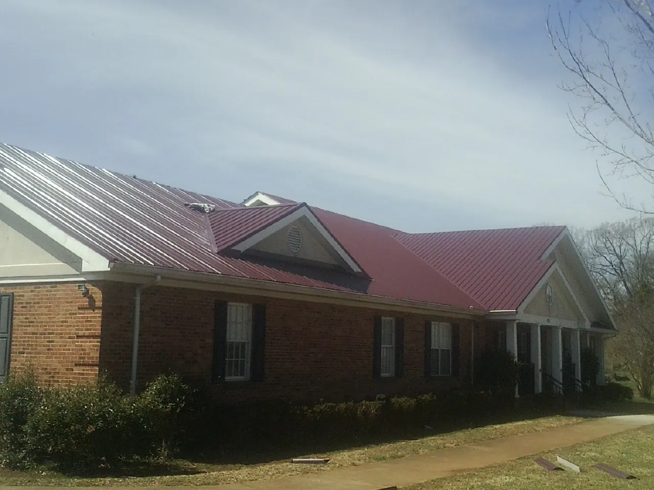 Red metal roof with gabled entries on a long brick building, from a Hail Damage Roof Repair job in Pomona Park