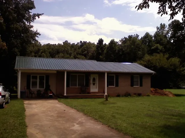 Dark green metal roof on a brick ranch with a covered porch in Pomona Park