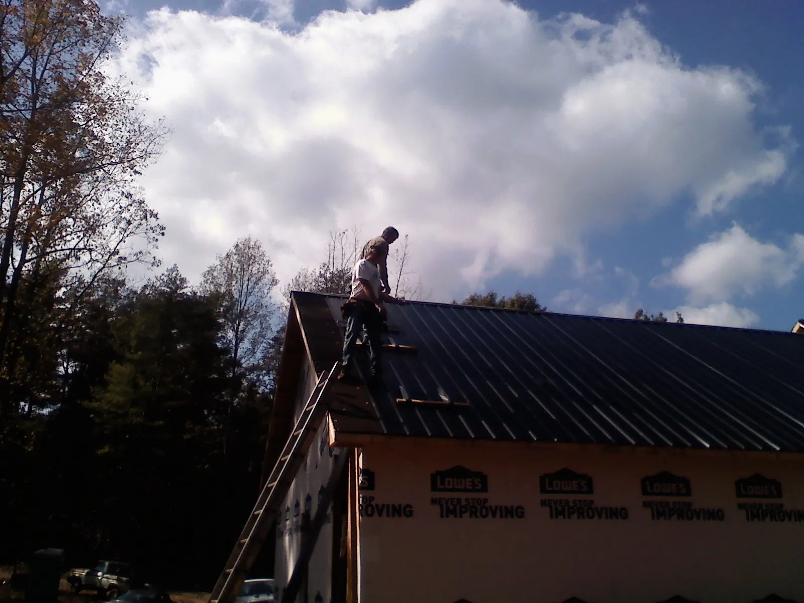 Roofer fastening dark metal panels high against a cloudy sky, from a Roof Inspection job in Pomona Park