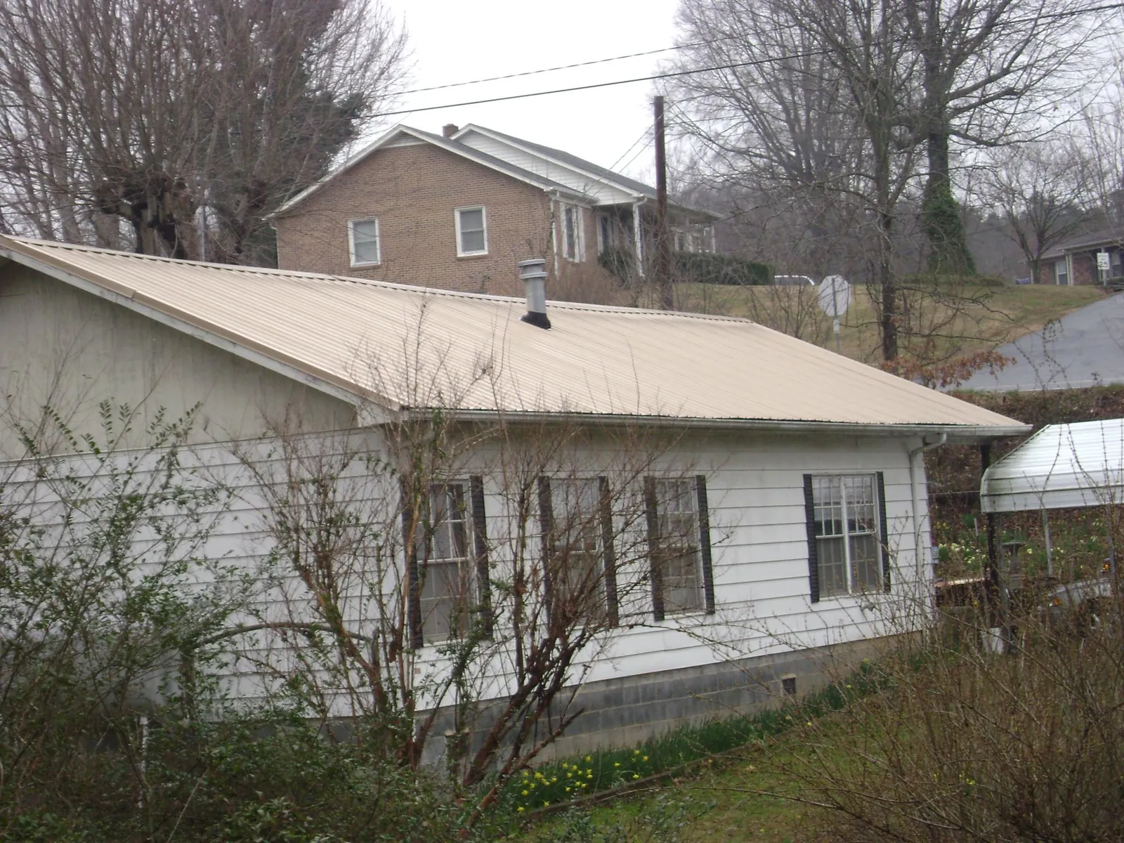 Tan metal roof on a white sided house set into a hillside — Commercial Roofing by Roofing Brothers in Pomona Park