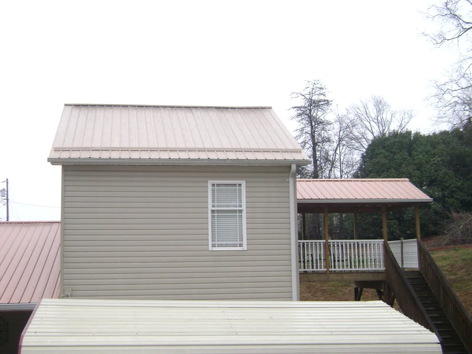 Tan metal roofs on a two story addition and attached porch, from a Roof Replacement job in Pomona Park